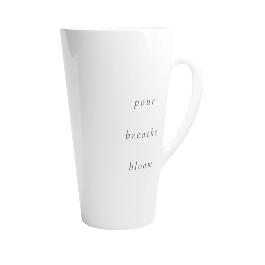 A tall white ceramic latte mug with the words 'pour breathe bloom' printed vertically.