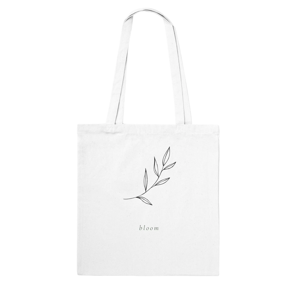 Tote bag with a delicate leafy branch design en the text 'bloom' beneath it.